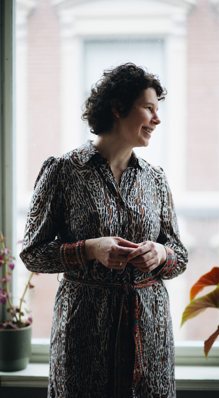 Foto van Christine in haar woonkamer, met het raam als achtergrond